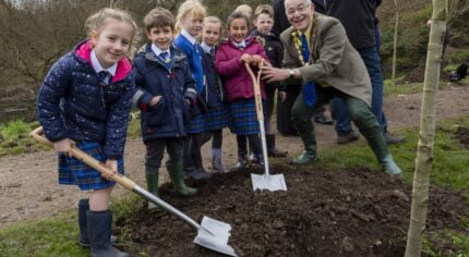 Small group of schoolchildren planting a tree with the Mayor