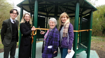 Four people with one cutting a ribbon across entrance to shelter