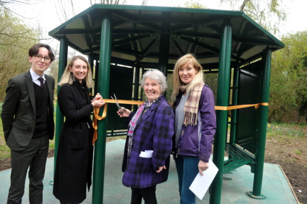 Four people with one cutting a ribbon across entrance to shelter