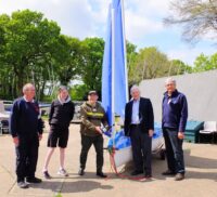 Five people standing in front of a sailing boat on land.