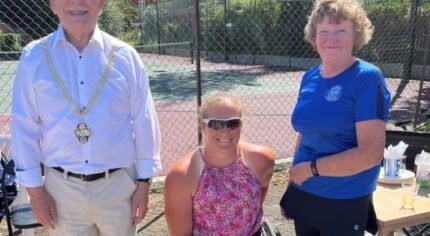 Three people in front of a tennis court.