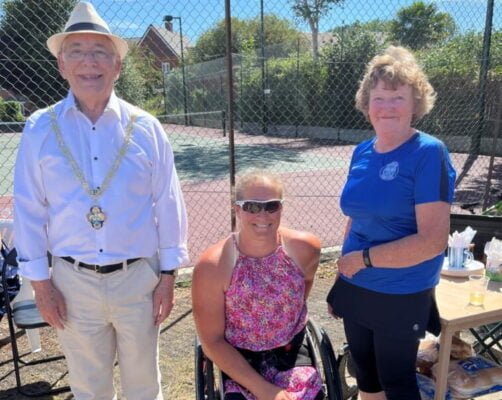 Three people in front of a tennis court.
