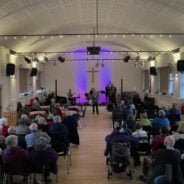 Inside the vineyard church looking down towards stage. Mayor of Farnham doing opening speech with crowd watching.