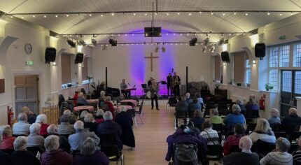 Inside the vineyard church looking down towards stage. Mayor of Farnham doing opening speech with crowd watching.