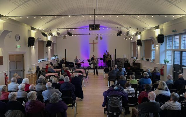Inside the vineyard church looking down towards stage. Mayor of Farnham doing opening speech with crowd watching.