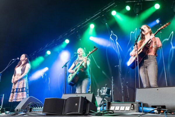 A photo featuring three women performing on stage, two with guitars and the other as main vocalist