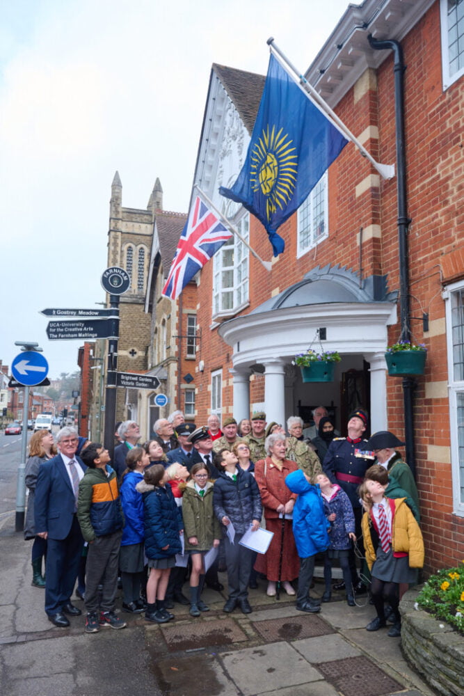 Group of adults and children looking up at a flag on the side of a building.