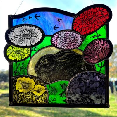 a STAINED GLASS ARTWORK FEATURING A HARE SURROUNDED BY FLOWERS IN BRIGHT COLOURS