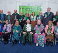 Two rows of people wearing medals on green ribbons.
