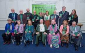 Two rows of people wearing medals on green ribbons.