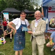 Lady in a paint splattered apron with Mayor holding a square of tie dyed material