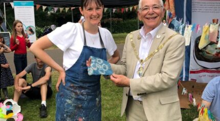 Lady in a paint splattered apron with Mayor holding a square of tie dyed material