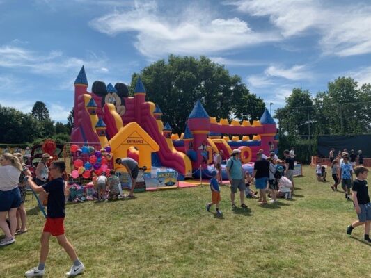 A photo showing a colourful bouncy castle at Wrecclesham recreation ground and people milling around at a previous Wrecclesham village fete