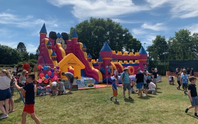 A photo showing a colourful bouncy castle at Wrecclesham recreation ground and people milling around at a previous Wrecclesham village fete
