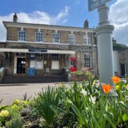 A photo showing Farnham station with flowers blooming in the forefront