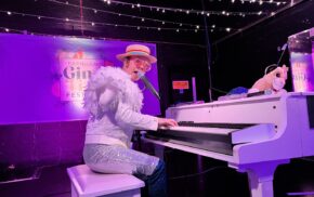 Man dressed in a white sparkly outfit playing a white grand piano.