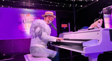 Man dressed in a white sparkly outfit playing a white grand piano.