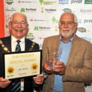 Mayor holding a certificate. Man on right of Mayor holding a glass trophy.