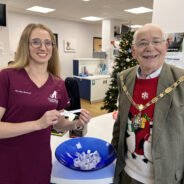 Smiling female in nurse's tunic and the Mayor draw a name from a blue bowl.