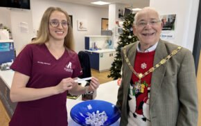 Smiling female in nurse's tunic and the Mayor draw a name from a blue bowl.