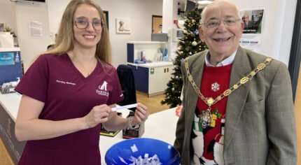 Smiling female in nurse's tunic and the Mayor draw a name from a blue bowl.