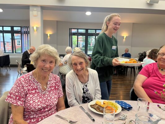 2 smiling ladies sitting at a table eating a roast dinner