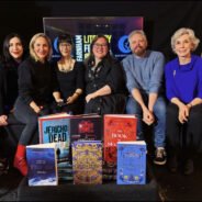 Six people sitting on a sofa with a display of books in the foreground.