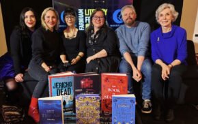 Six people sitting on a sofa with a display of books in the foreground.