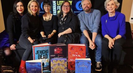 Six people sitting on a sofa with a display of books in the foreground.