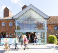 Red brick building with glass porch and people walking around.