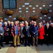 Group of people in front of a wall showing a number of commemorative plaques.