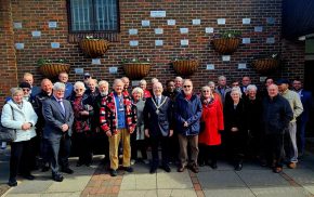 Group of people in front of a wall showing a number of commemorative plaques.