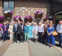 Group of people standing in front of a brick wall displaying commemorative plaques.