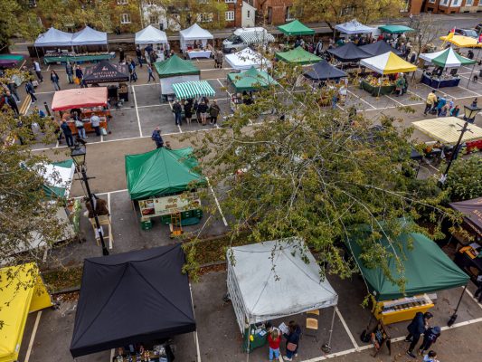Aerial view of rows of different coloured market stalls in a car park