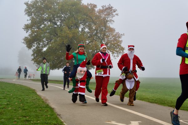 A group of people running along a path in a park on a foggy day. Some are wearing Santa costumes.