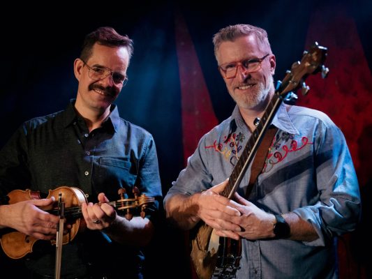 Two men smiling at the camera holding musical instruments