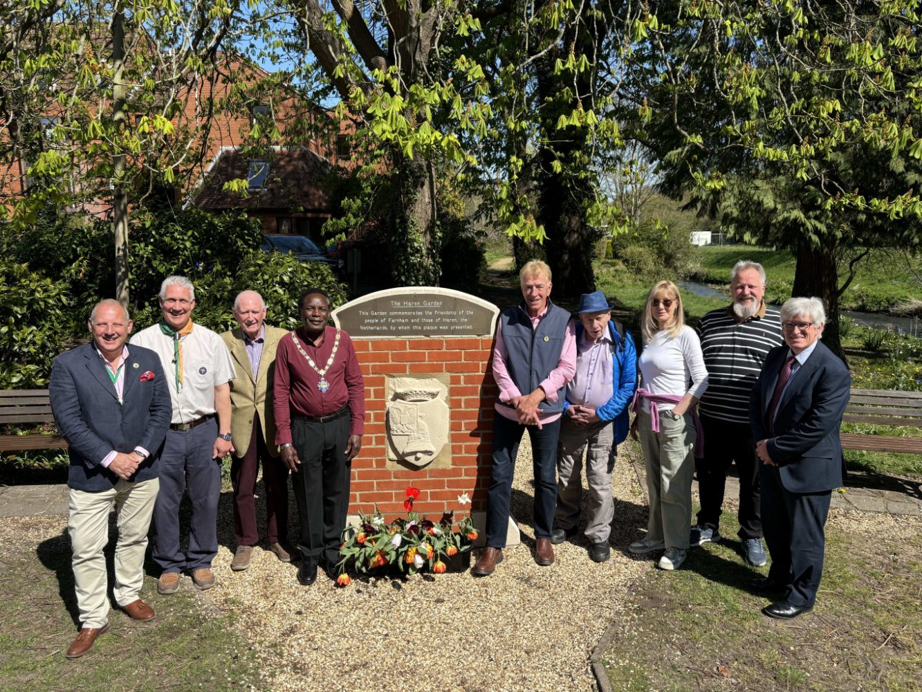Group of people standing either side of a plaque mounted on a brick wall.