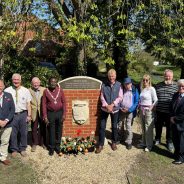 Group of people standing either side of a plaque mounted on a brick wall.