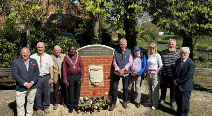 Group of people standing either side of a plaque mounted on a brick wall.