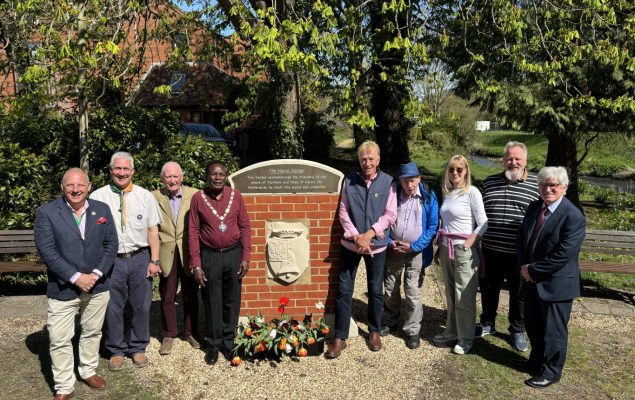 Group of people standing either side of a plaque mounted on a brick wall.