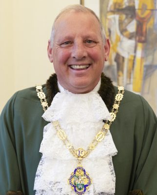 Smiling man dressed in a green Mayoral robe, a white lace jabot and gold chain of office.