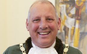 Smiling man dressed in a green Mayoral robe, a white lace jabot and gold chain of office.