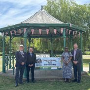 Four people standing either side of a banner attached to a band stand.