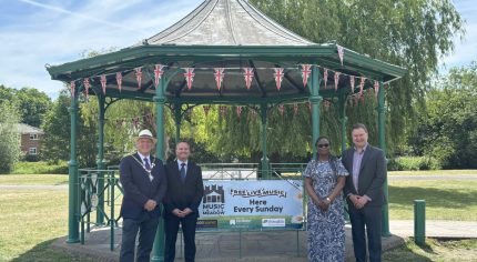 Four people standing either side of a banner attached to a band stand.