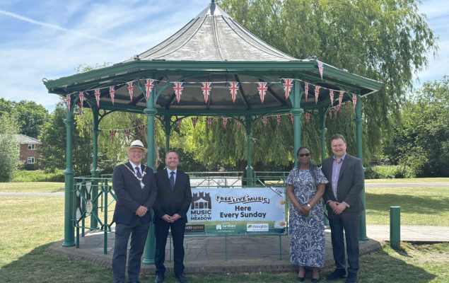 Four people standing either side of a banner attached to a band stand.