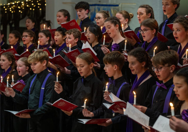 Young people singing by candlelight in a choir.