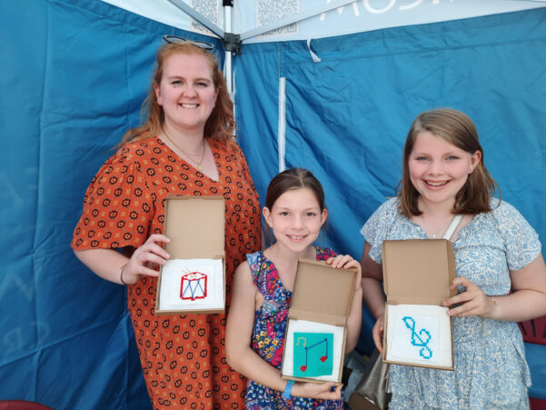 Woman and two girls showing a cross stitch sample.