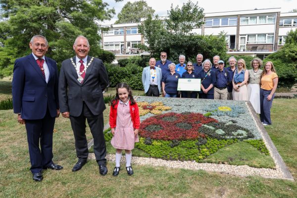 Group of people admiring a carpet bed showing a ladybird made out of plants.