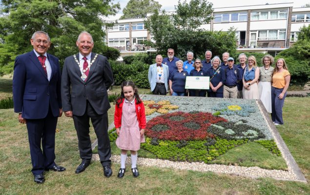Group of people admiring a carpet bed showing a ladybird made out of plants.