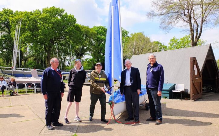 Five people standing in front of a sailing boat on land.